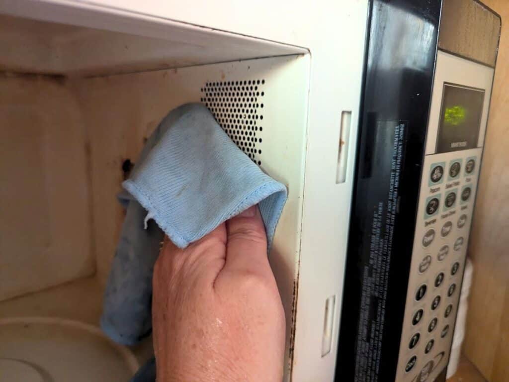  Image shows a Hand cleaning a microwave with a cloth.