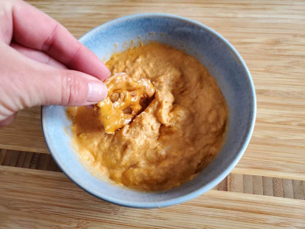 Image shows pretzel dip into buffalo chicken dip in a bowl.