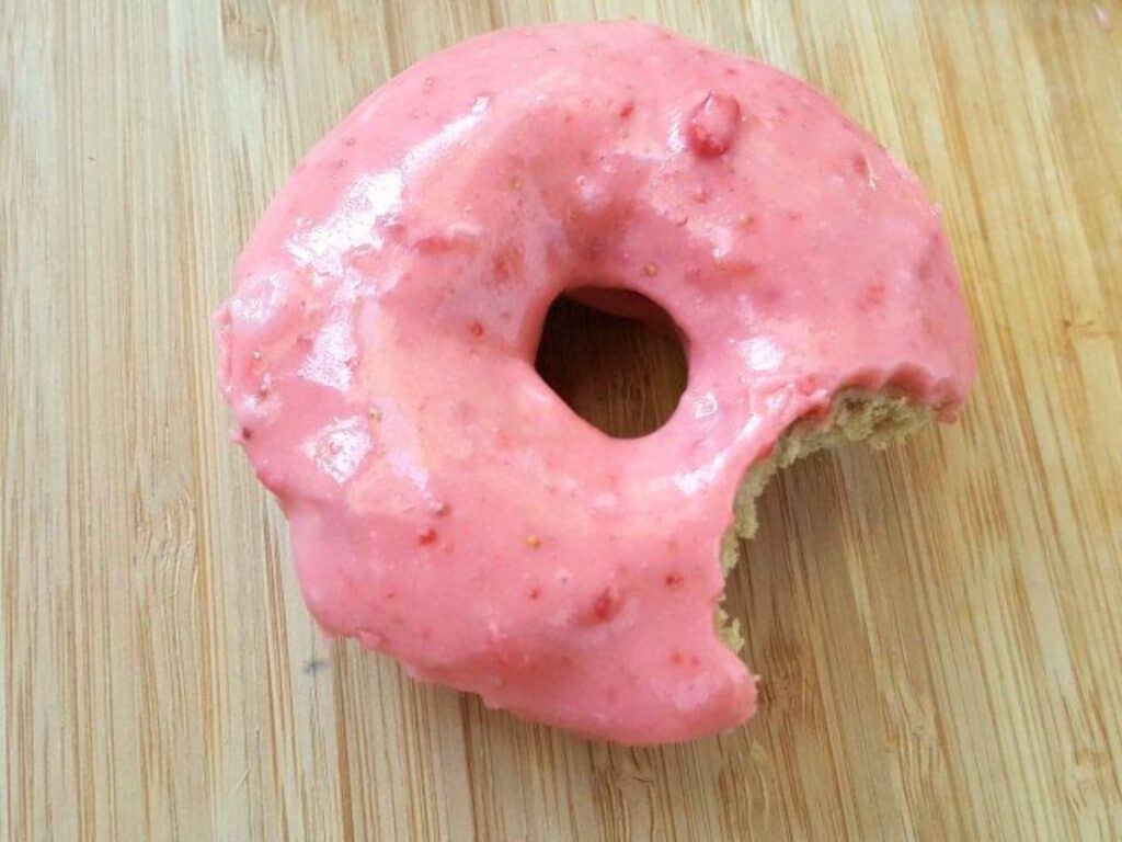 Image shows yummy and homemade strawberry donut with a bite missing.
