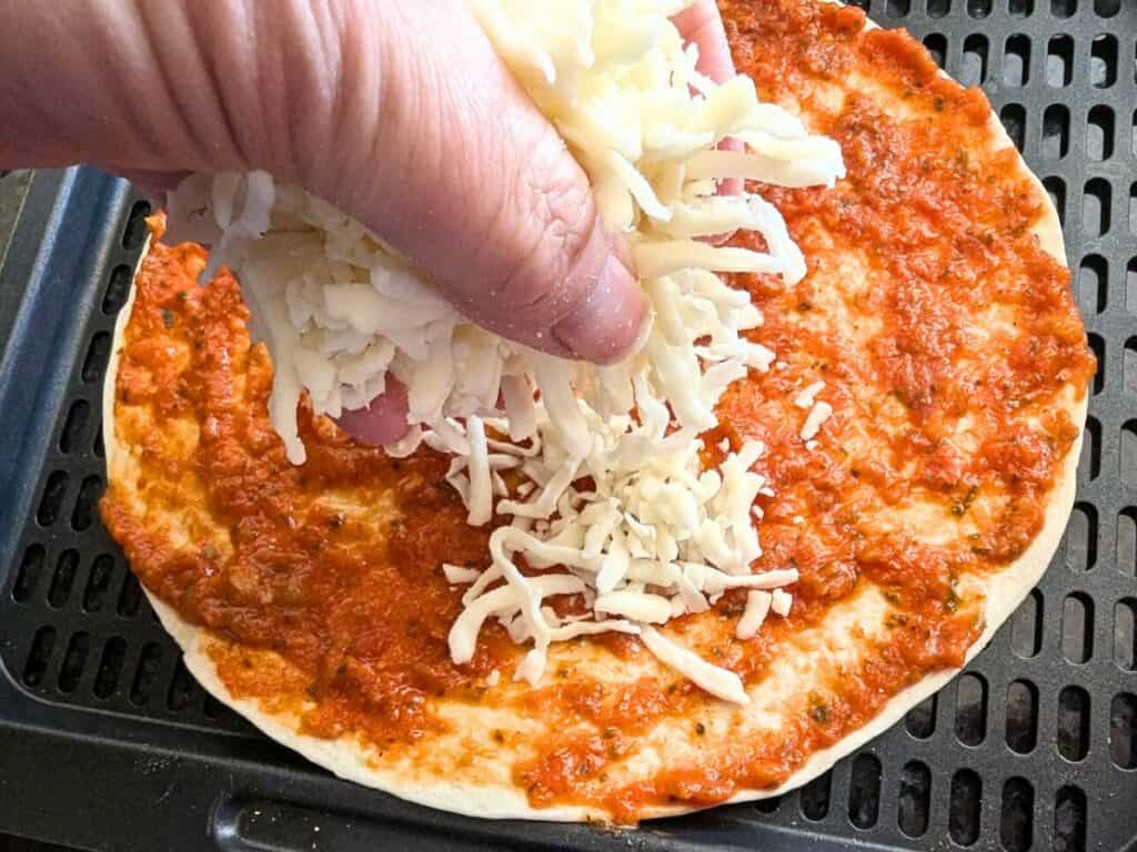 Image shows adding mozzarella cheese on top of the tomato sauce.