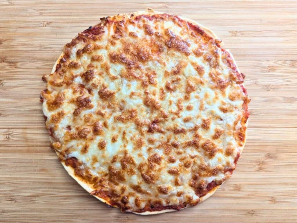 Image shows cooked tortilla pizza on a wooden tray.