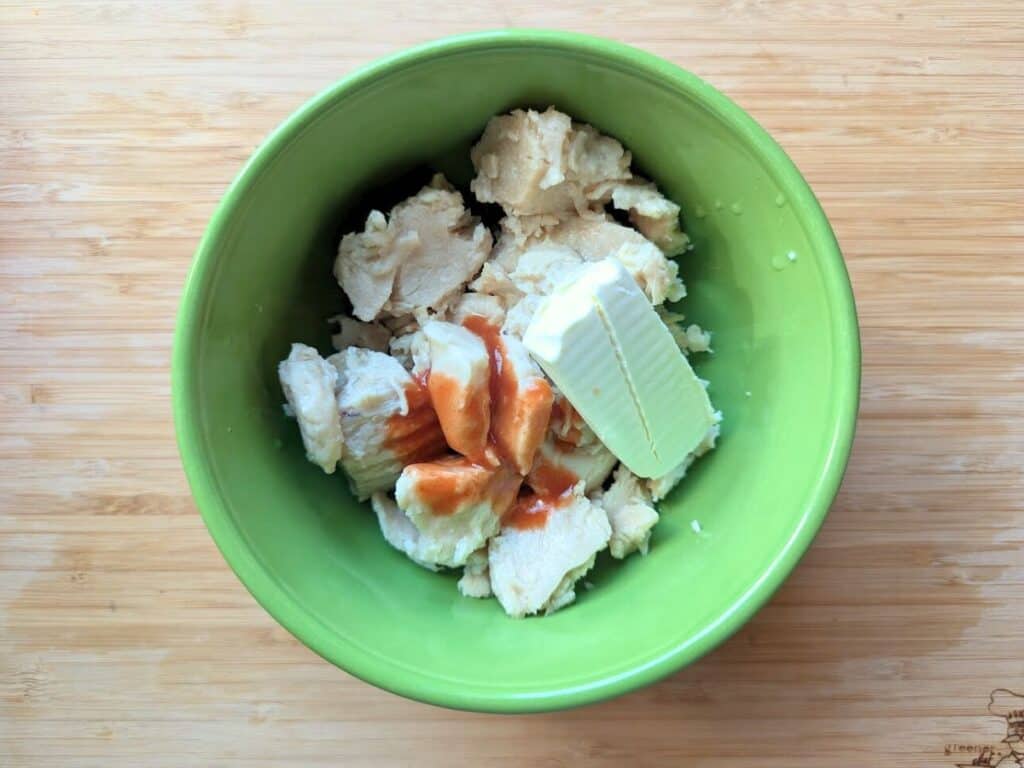 Image shows buffalo chicken salad ingredients in a bowl, including canned chicken, hot sauce, and dressing..
