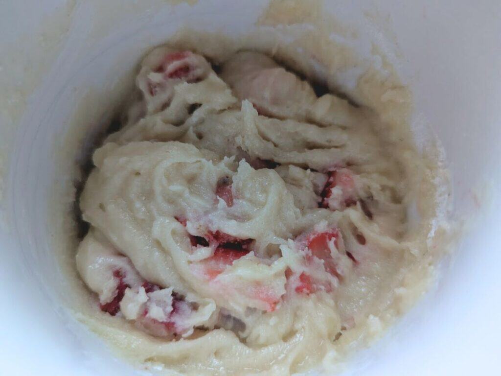 Image shows chopped strawberries added to the mug and mixed into the batter.