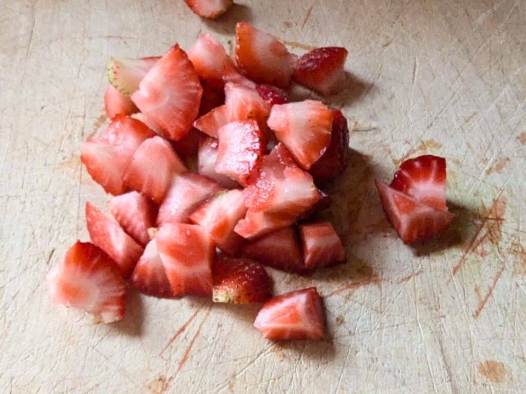 Image shows chopped strawberries on a wooden chopping board.