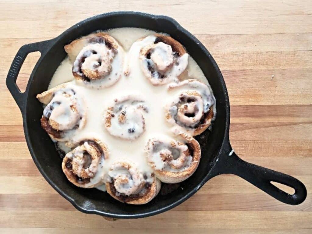 Image shows delicious cinnamon rolls in cast iron pan.