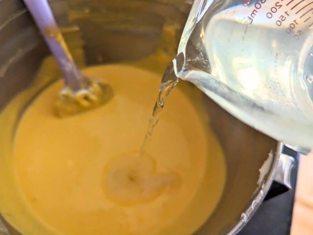 Image shows pouring gelatin water into the mango mixture for mango mousse.
