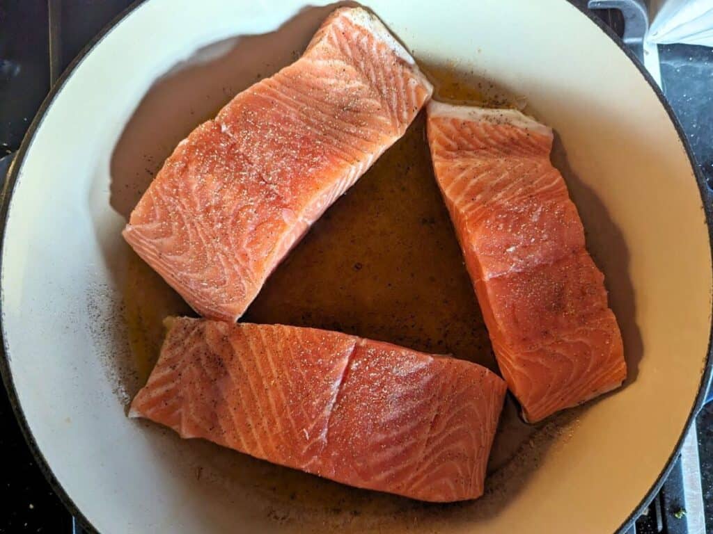 Image shows searing the salmon fillets seasoned with salt and black pepper.