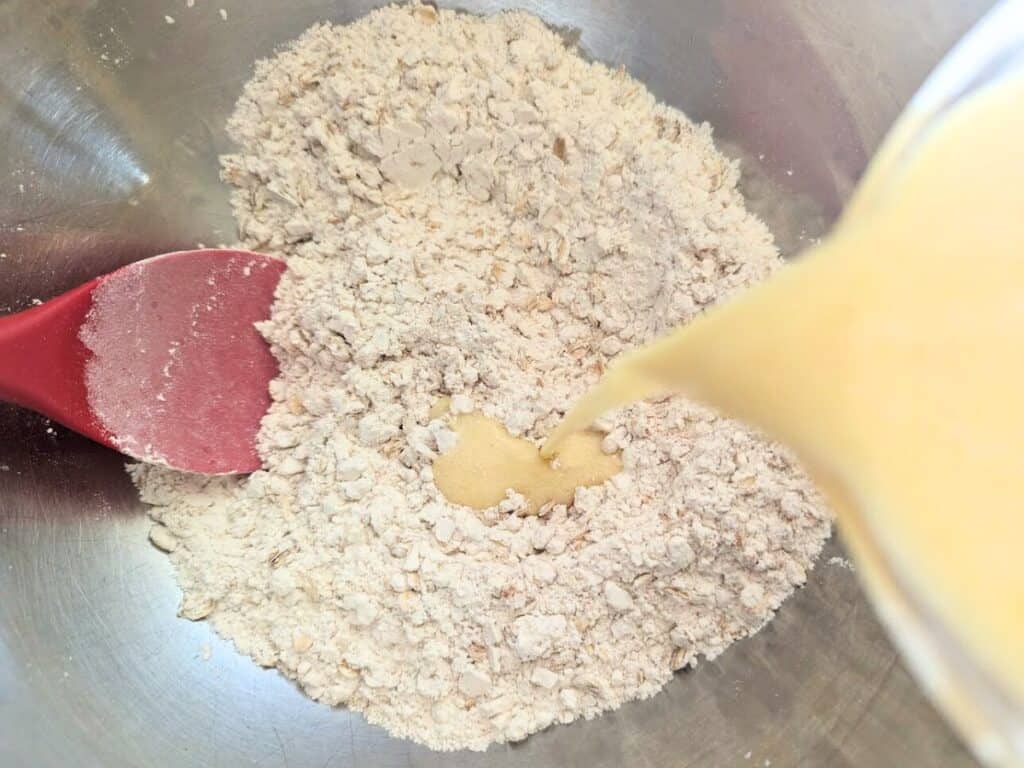 Image shows Wet ingredients being poured into the dry ingredients for apple scones.