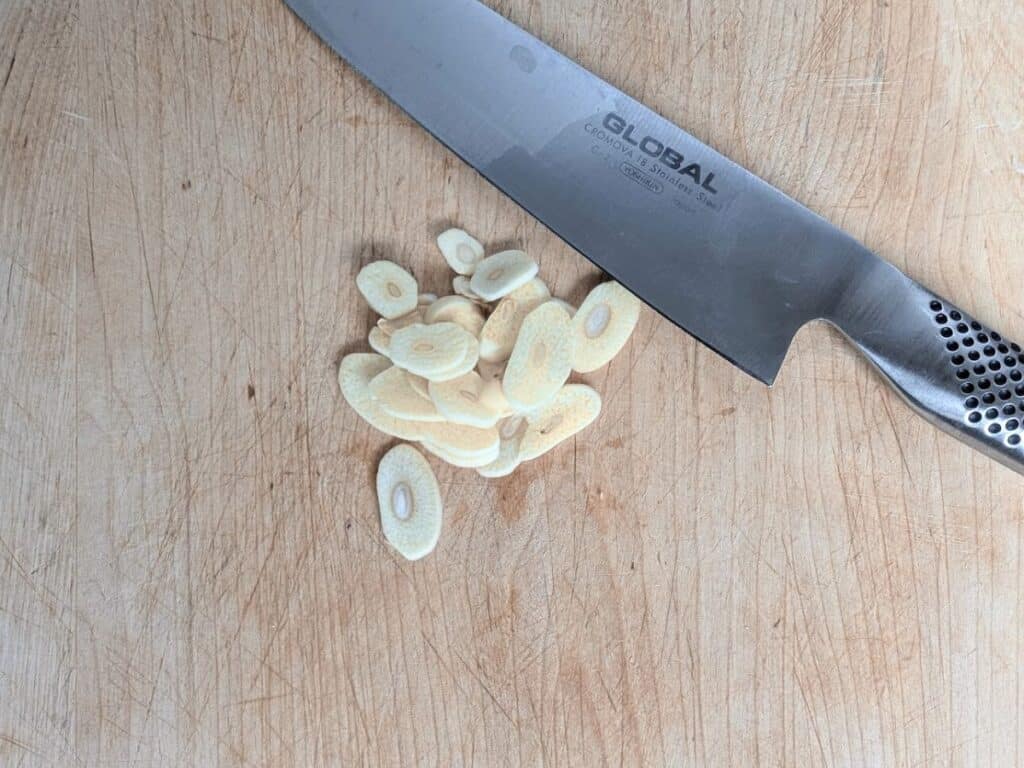 Image shows  A small pile of freshly sliced garlic on a cutting board.