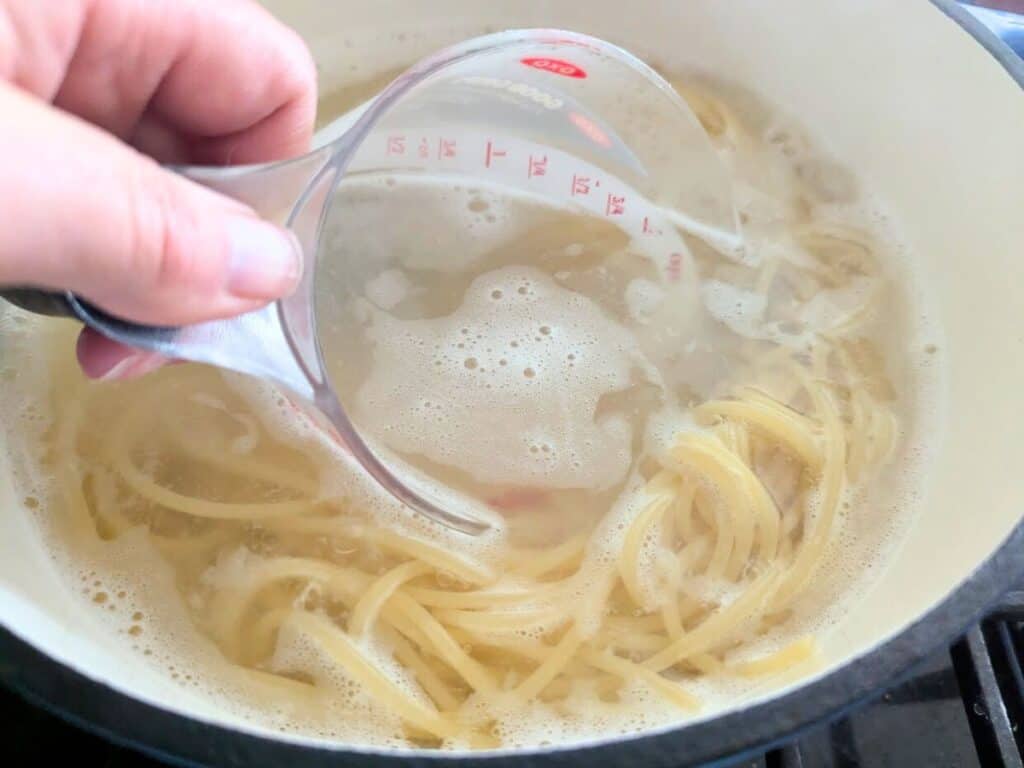 Image shows a liquid measuring cup Collecting hot pasta water from a pot before draining the noodles.
