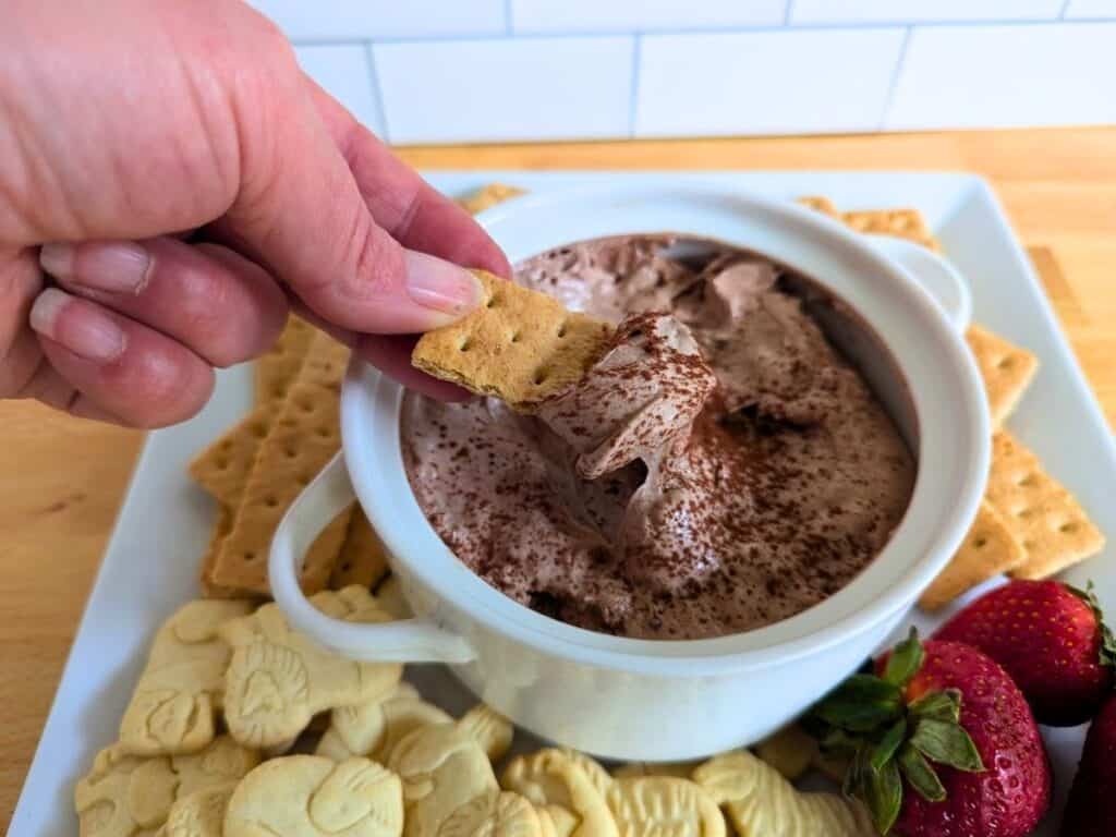 Image shows hand holding a cracker with hot chocolate dip on it.