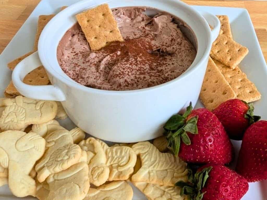 Image shows hot chocolate dip served with graham crackers, biscuits, and strawberries.