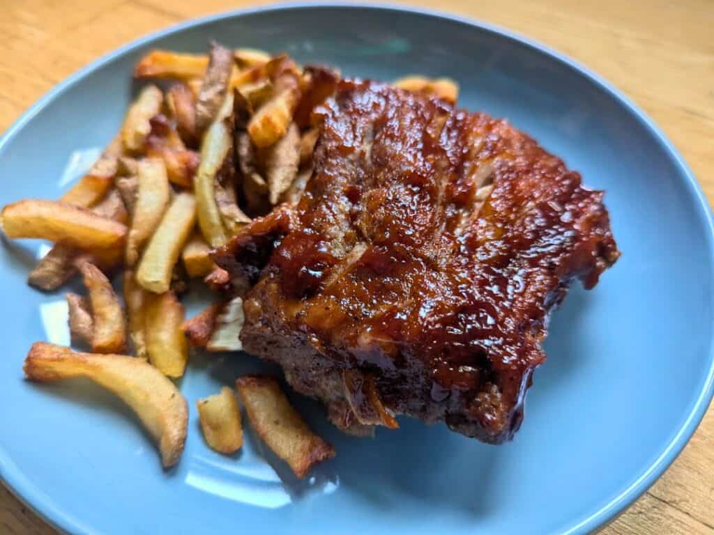Image shows close-up of a slice of baby back ribs with fries on a blue plate.