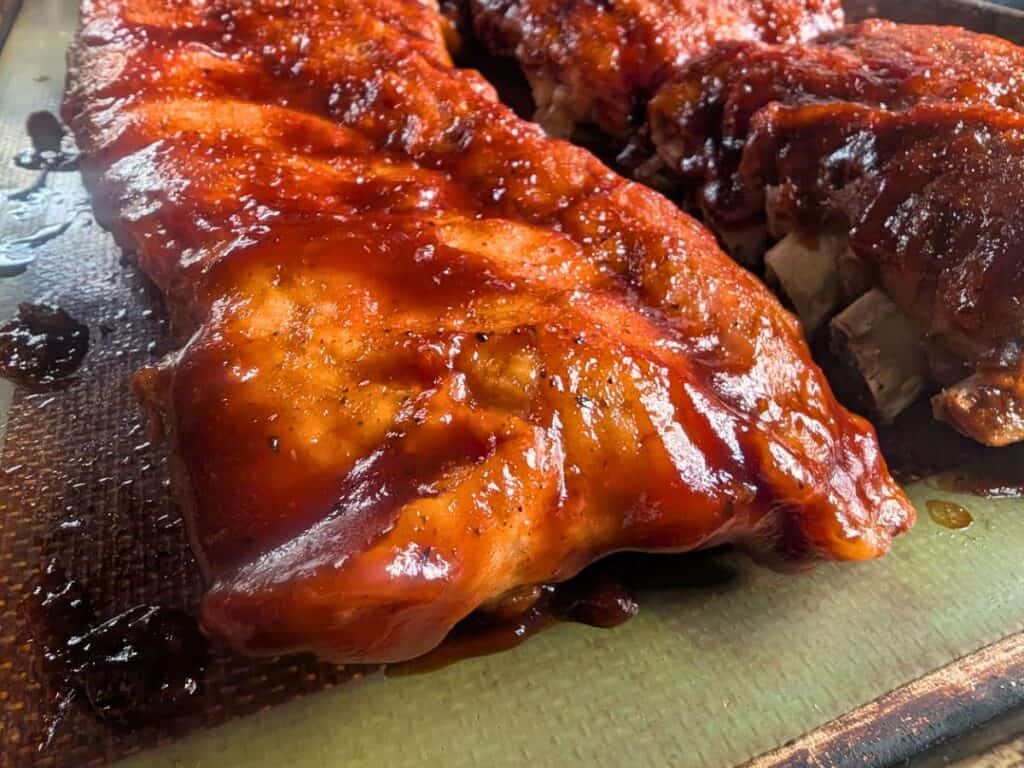 Image shows cooked baby back pork ribs placed on a Silpat-lined baking sheet.