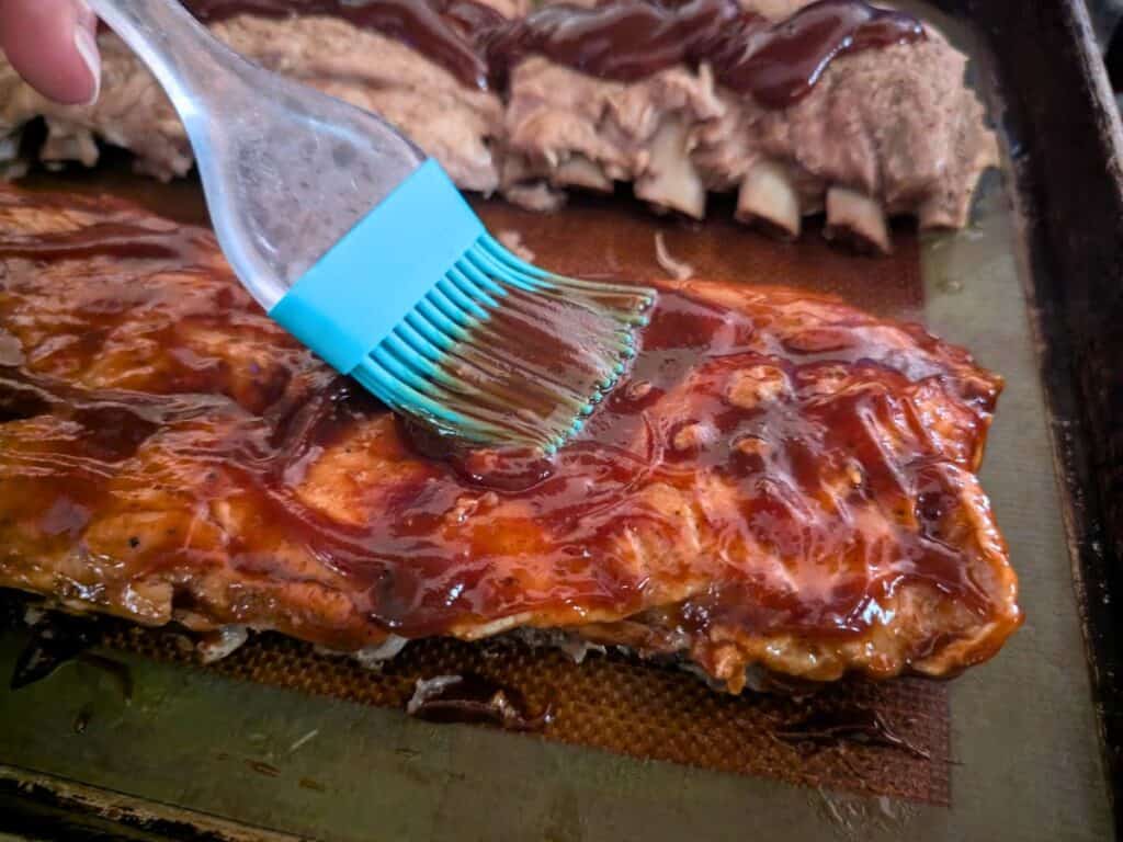 Image shows sliced pork ribs on a Silpat mat, brushed with barbecue sauce.