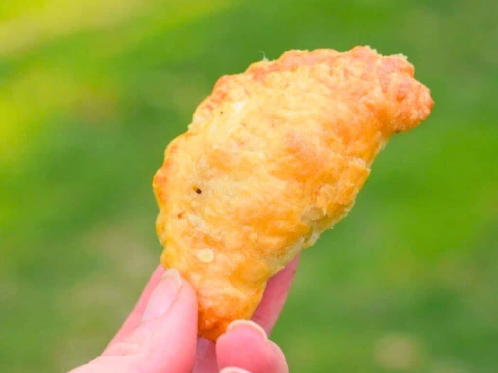 Image shows hand holding an irresistible puff pastry beef empanada.