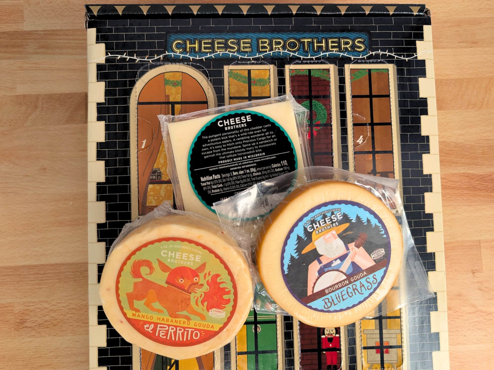 Three packages of Cheese Brothers cheese, including Mango Habanero Gouda and Bourbon Gouda, arranged on an advent calendar box.