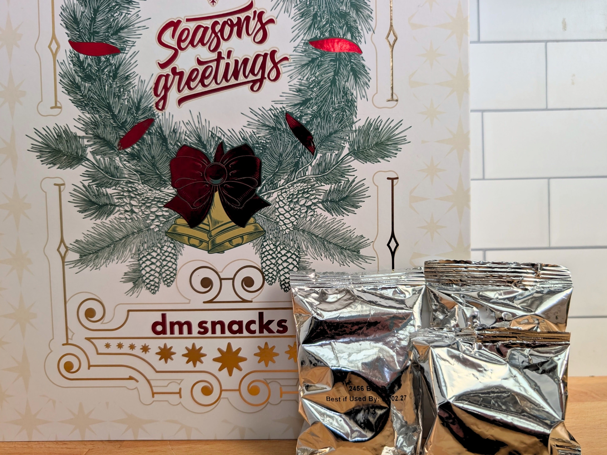 Two silver snack pouches in front of a holiday-themed &ldquo;Season&rsquo;s greetings&rdquo; dm snacks box.