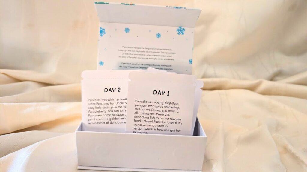 A white box with story cards labeled "Day 1" and "Day 2" stands upright on a light-colored fabric surface, evoking the charm of Advent calendars with its daily surprises and printed text.