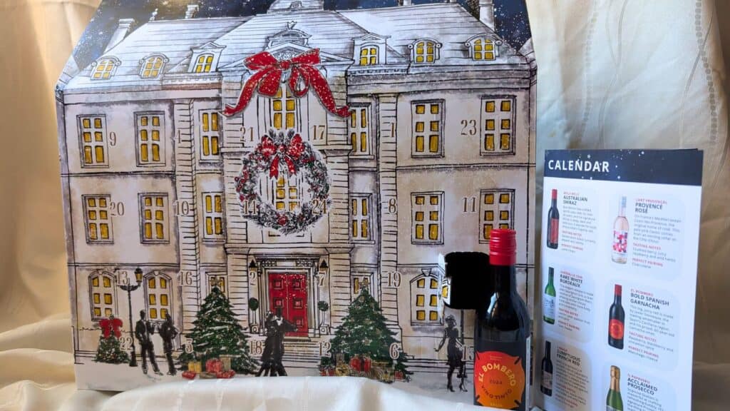 A festive advent calendar shaped like a decorated mansion stands beside a small bottle of Bombay Sapphire gin and an informational card listing drinks.