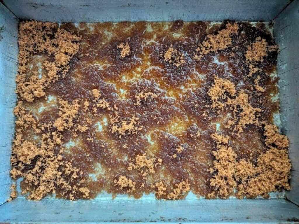 A rectangular metal tray containing a layer of crystallized brown sugar, reminiscent of the glossy topping on a pineapple upside down cake, with uneven clusters and a caramelized surface.