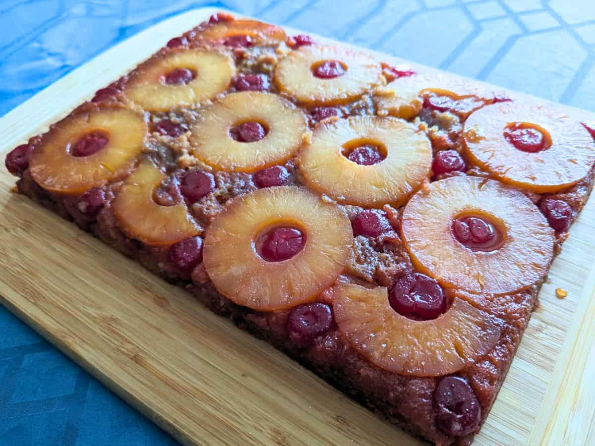 A rectangular pineapple upside down cake with pineapple rings and cherries, beautifully displayed on a wooden cutting board.