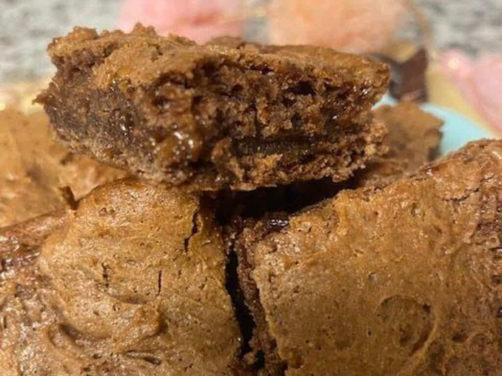 Close-up of chocolate brownies stacked on top of each other, with one brownie showing a moist and fudgy interior.