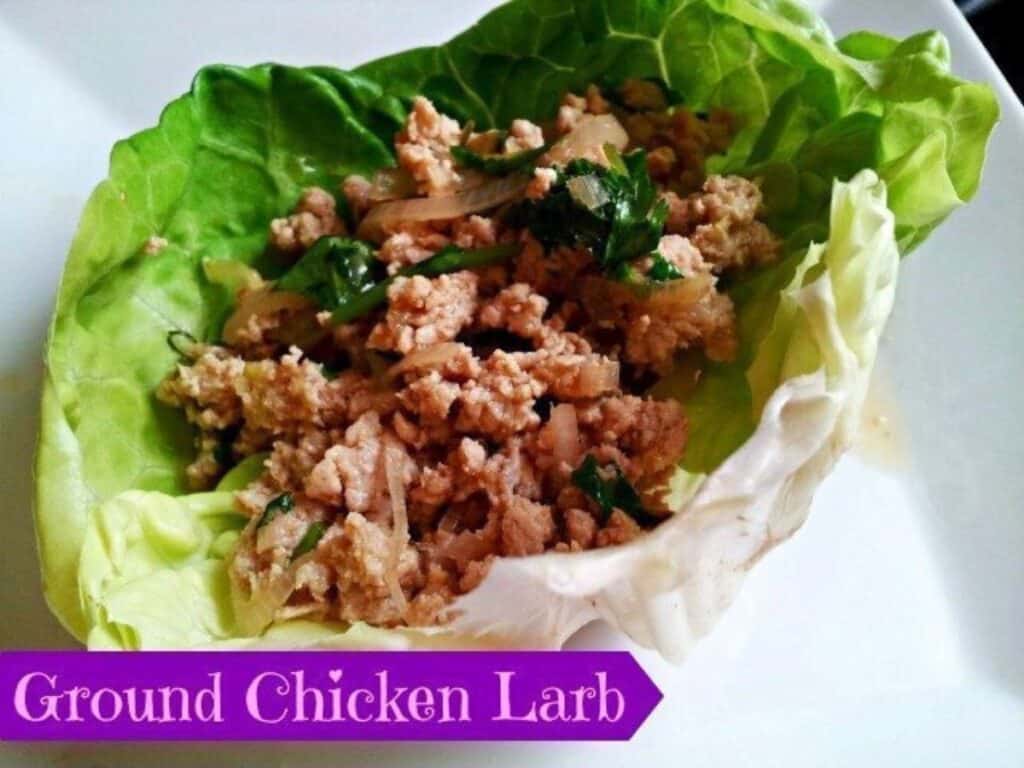 A lettuce leaf filled with ground chicken larb, garnished with herbs, on a white plate. A label at the bottom reads "Ground Chicken Larb.