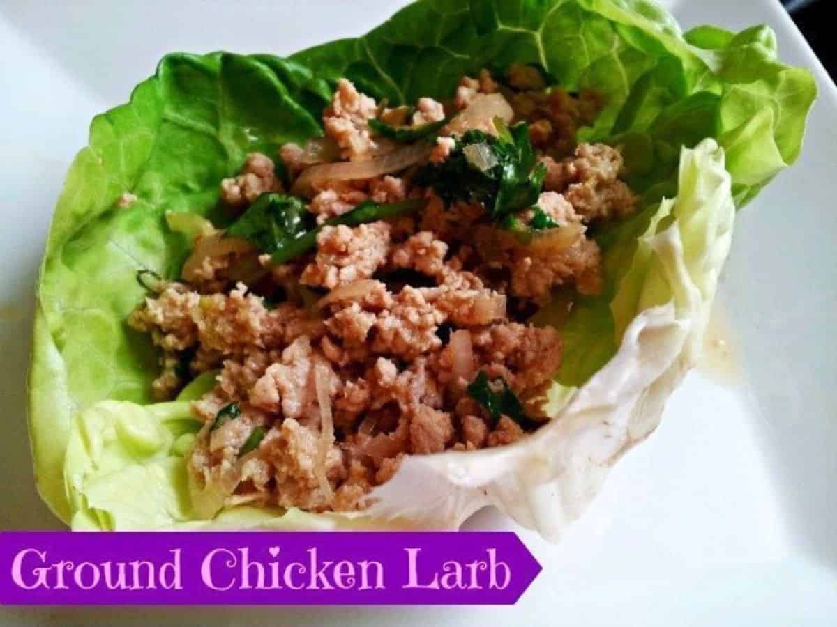 A lettuce leaf filled with ground chicken larb, garnished with herbs, on a white plate. A label at the bottom reads "Ground Chicken Larb.