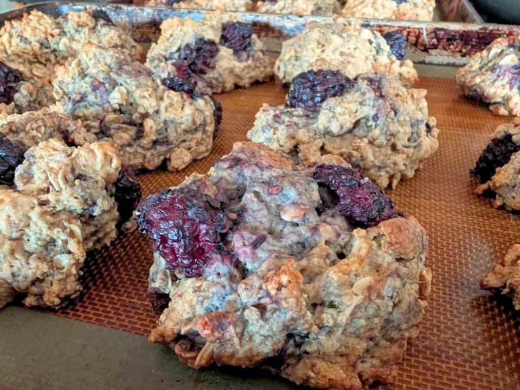 Close-up of several oat scones with visible blackberries, arranged on a brown silicone baking mat on a baking sheet.