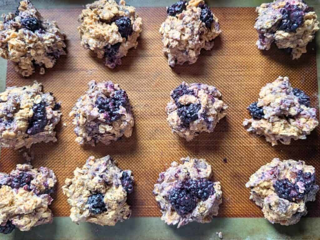 Twelve unbaked blackberry oatmeal scones arranged on a silicone baking mat, ready to be baked.