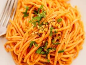 Plate of spaghetti with red sauce, garnished with chopped parsley and crushed nuts, with a fork on the side.