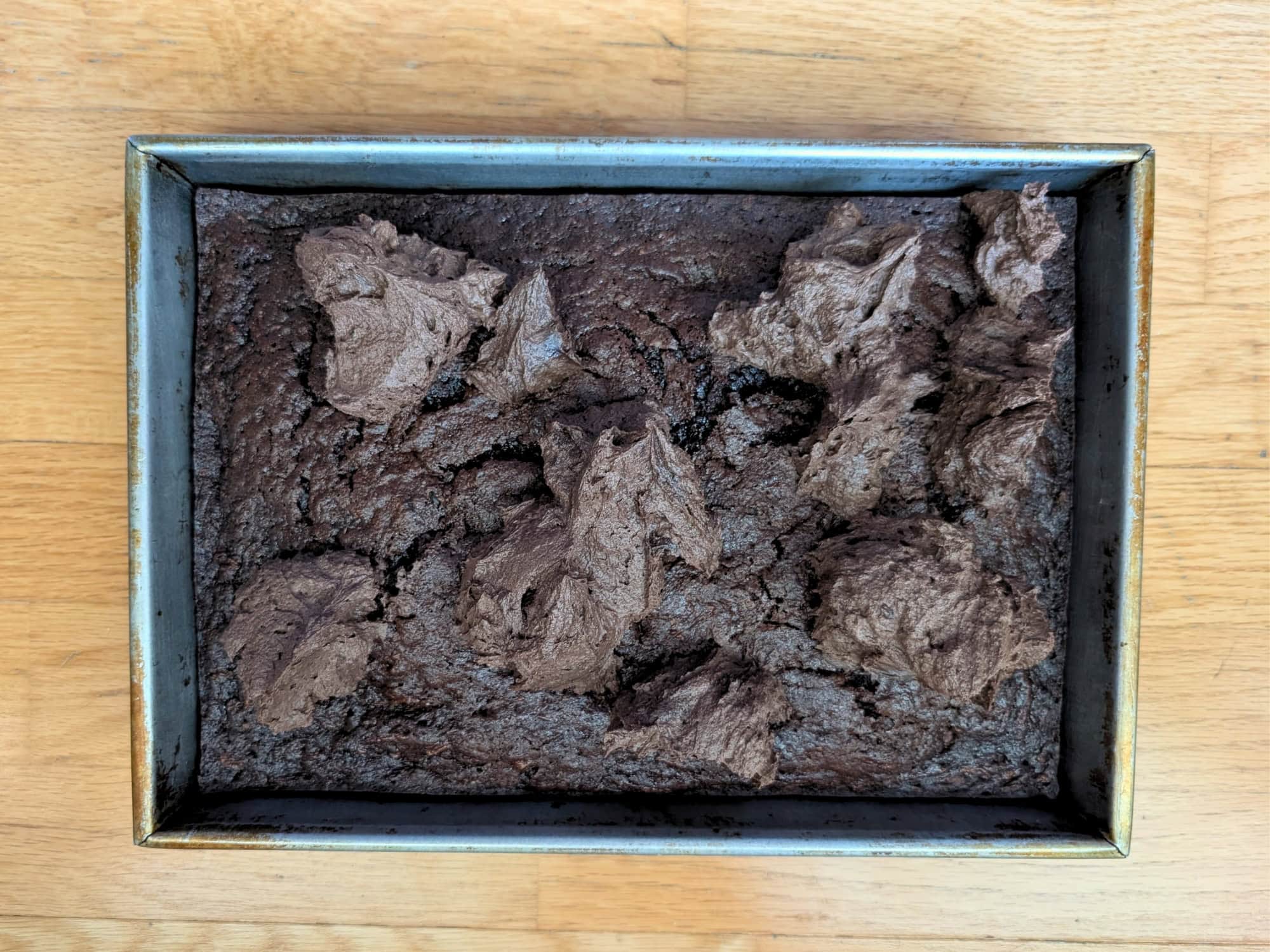 Dollops of chocolate frosting on a cooled chocolate zucchini cake in a 9x13 pan.