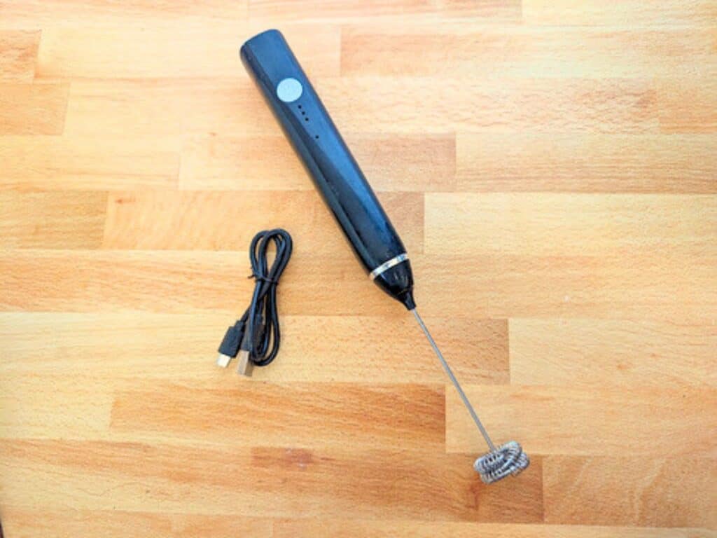 Black handheld electric milk frother and a USB charging cable on a wooden surface.