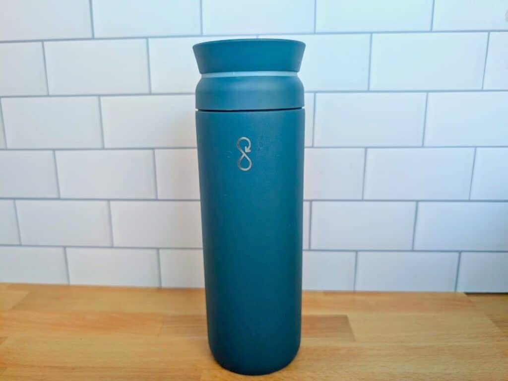 A teal reusable travel mug with an infinity loop logo on the front.