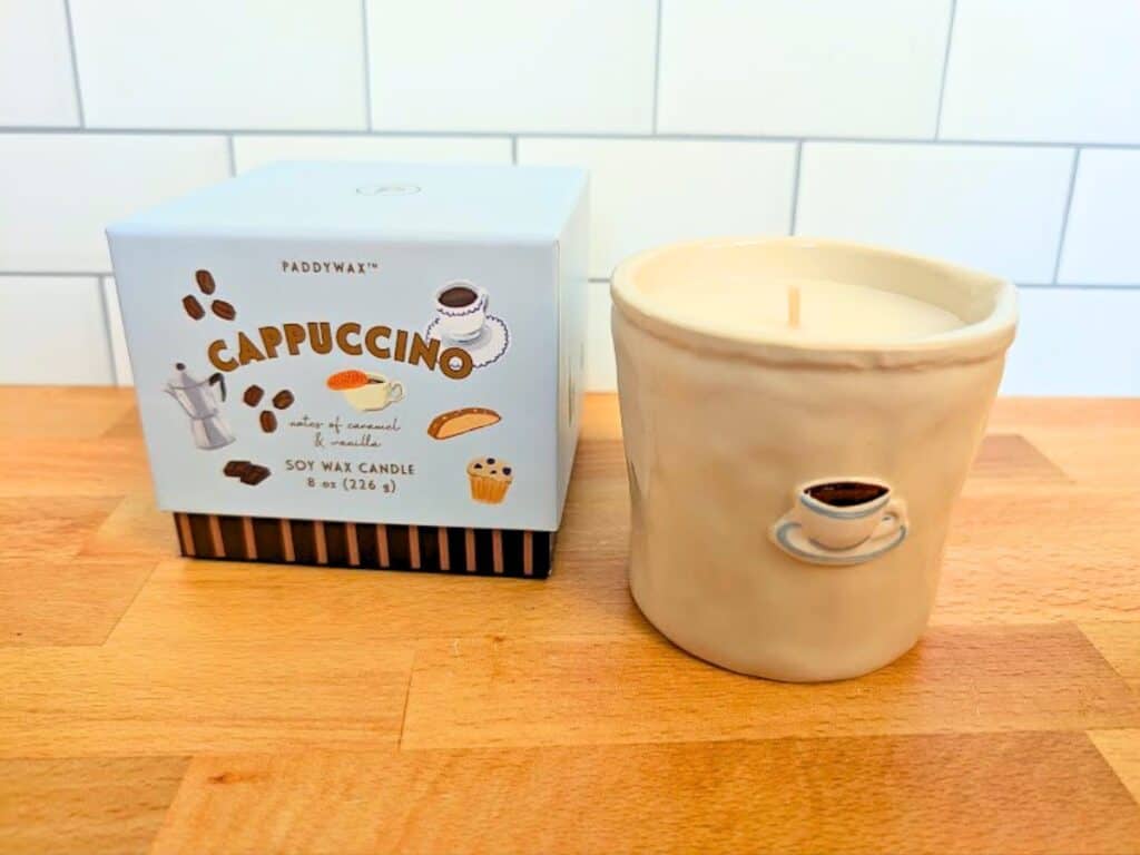 Paddywax Cappuccino soy wax candle in a ceramic mug with a matching box on a wooden surface.