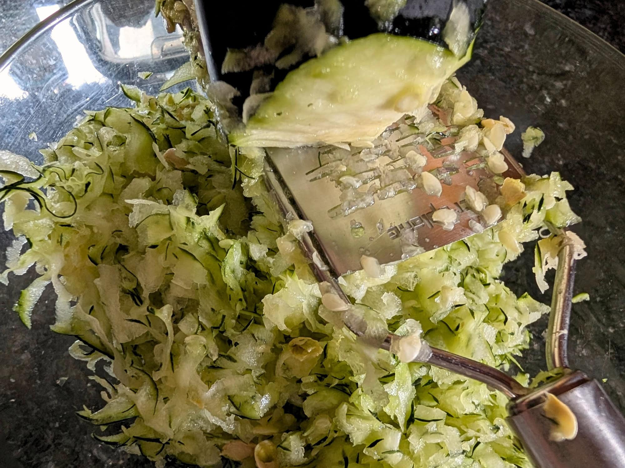 Shredding zucchini with a ribbon grater into a glass bowl for chocolate zucchini cake.