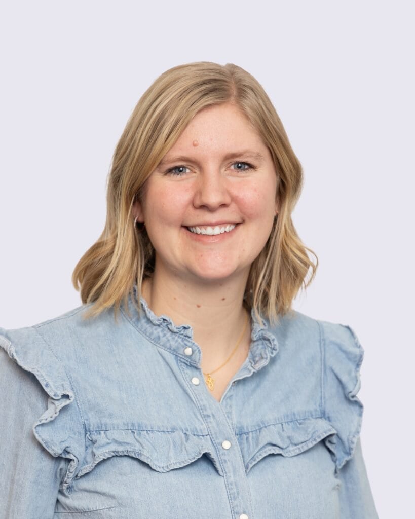 Kvindelig professionel i denimskjorte med blødt smil, neutral baggrund.