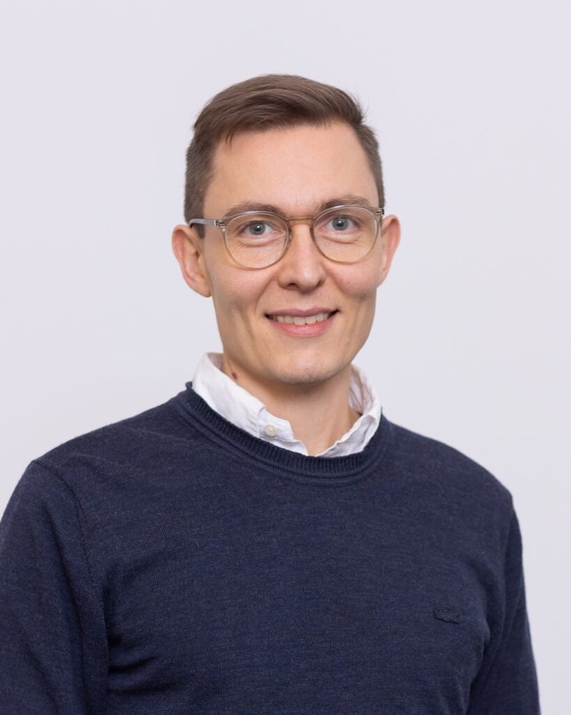 Menneske i smart casual tøj med briller, smilende, professionel portrætfoto.