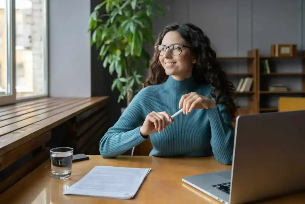 Kvindelig medarbejder i fokus, arbejder positivt i moderne kontor med naturligt lys og grøn plante.