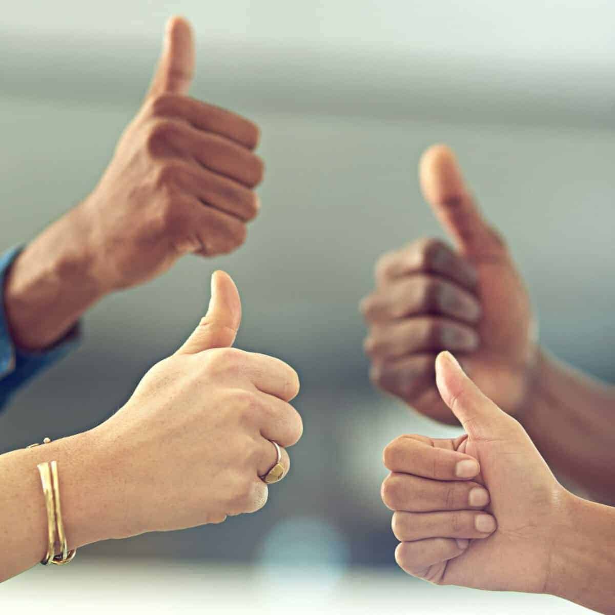 Smilende hænder giver tommelfinger op, symbol på positivitet, teamarbejde og succes.