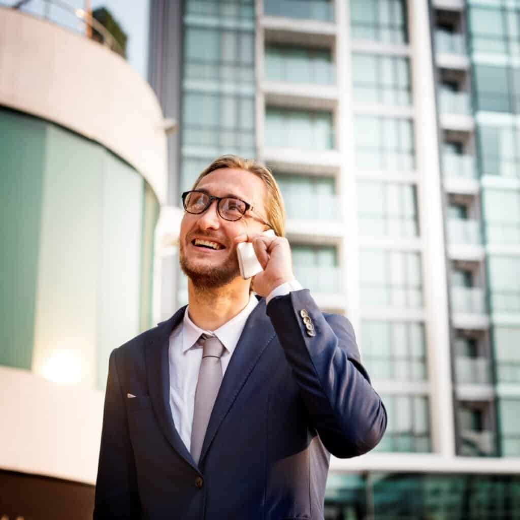 Mænd i forretningsdragt taler i telefon udendørs foran moderne bygning.
