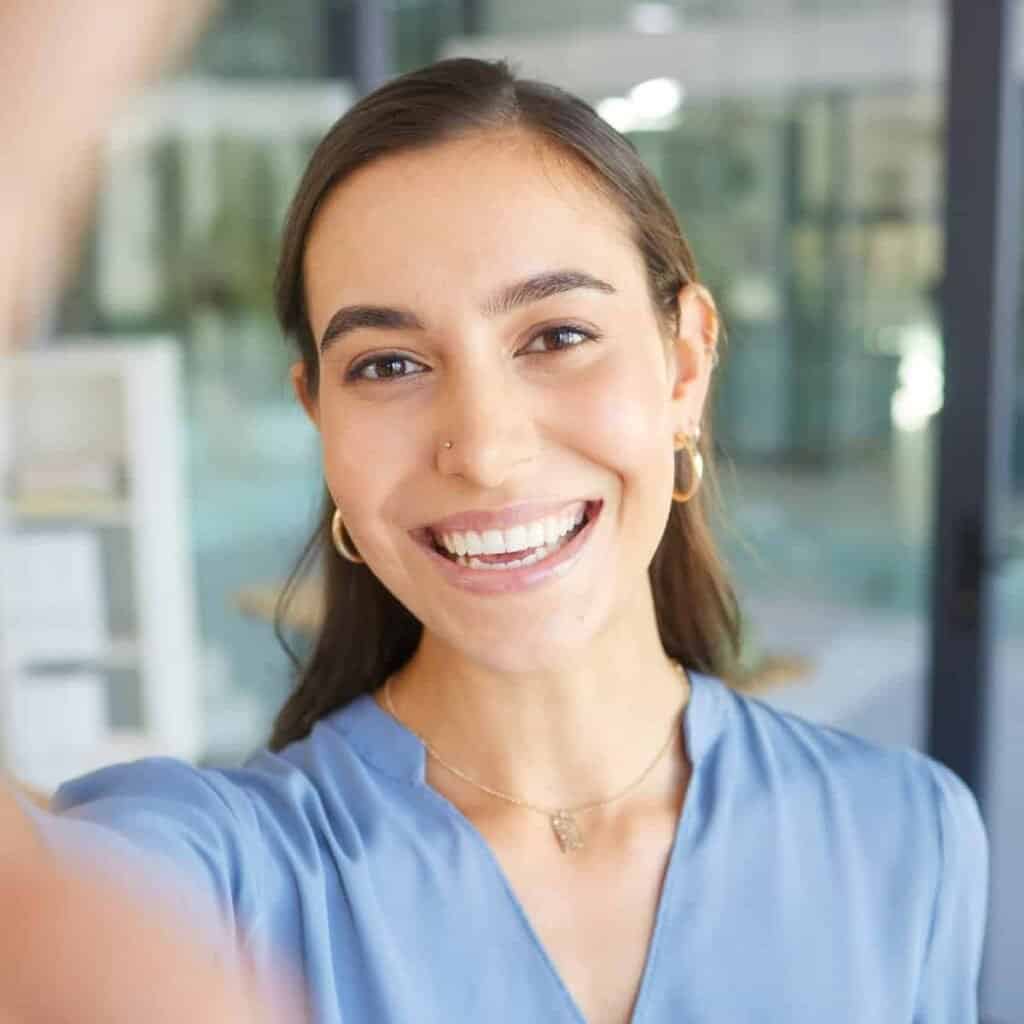 Smilende ung kvinde tager selfie, indendørs, professionel, glad, moderne kontor, positiv energi.