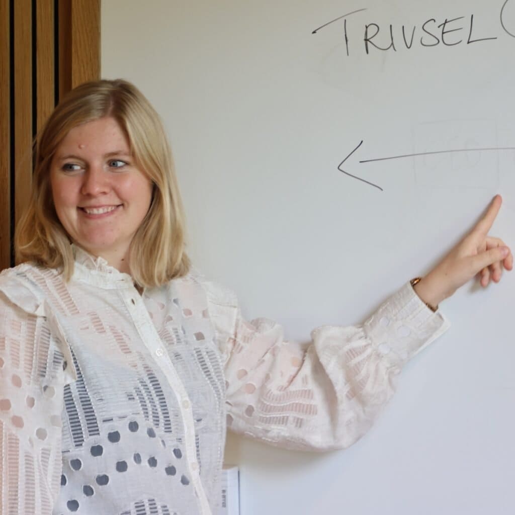 Engageret kvinde peger på whiteboard med "Troubel" skrift og diagram, illustrerer problemløsning og teamwork.