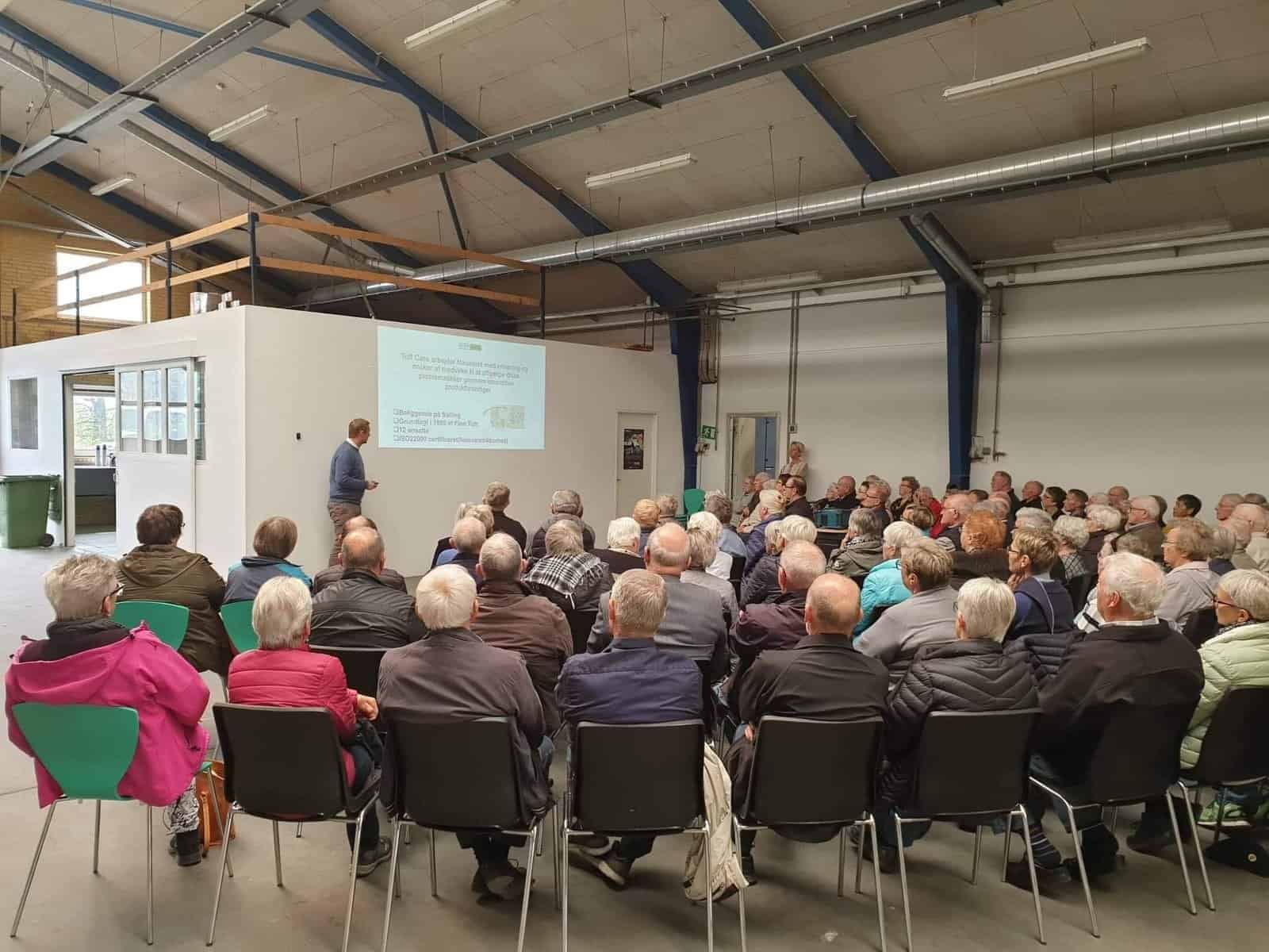1. Mennesker til foredrag i industriel lokation, fokus på seniorer og samfundsengagement.