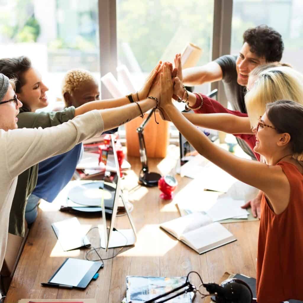 Gruppe mennesker der fejrer succes med high five i et mødelokale.