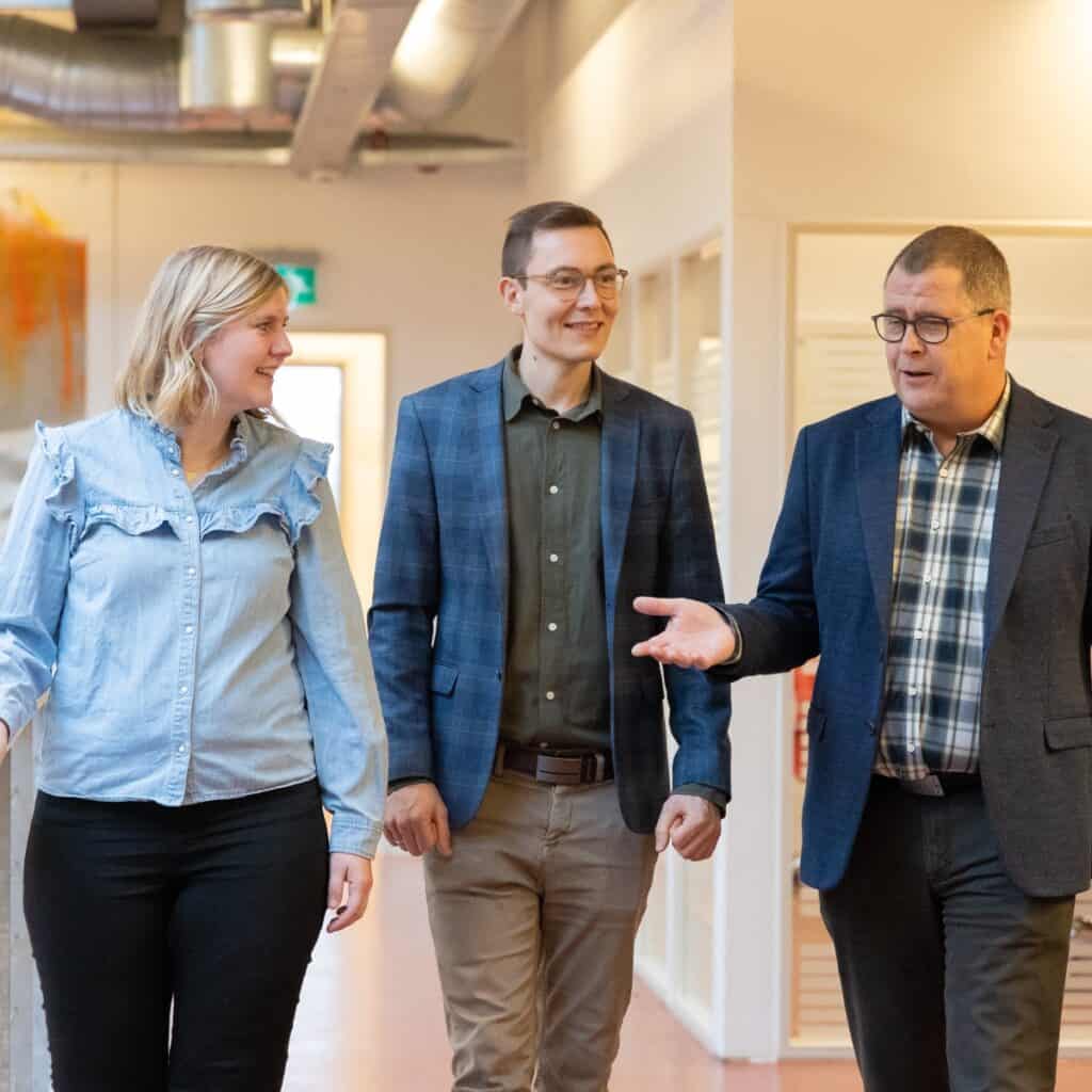 Tre personer i samtale på kontor, smilende og engagerede.
