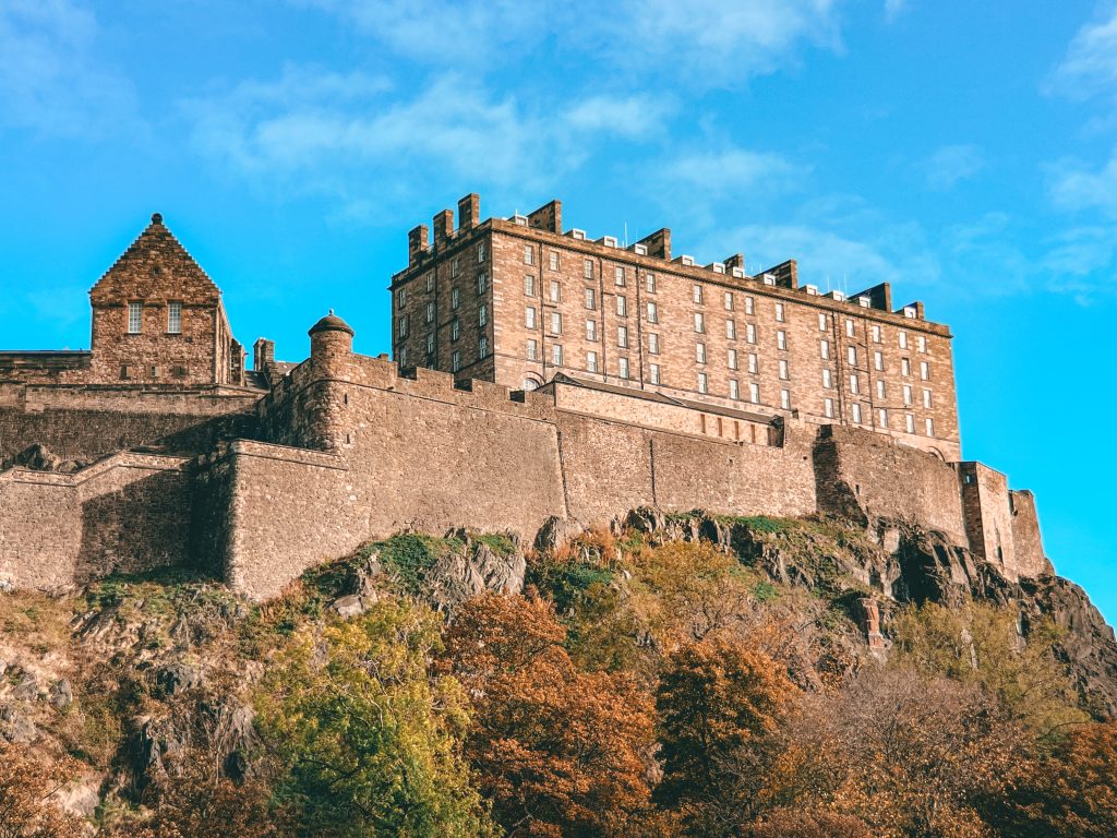 Edinburgh Castle with a blue sky above and rocks and trees below