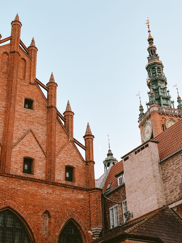 Discover the charm of a weekend in Gdańsk with its gothic red brick buildings, pointed roofs, and a towering clock tower under the clear sky.