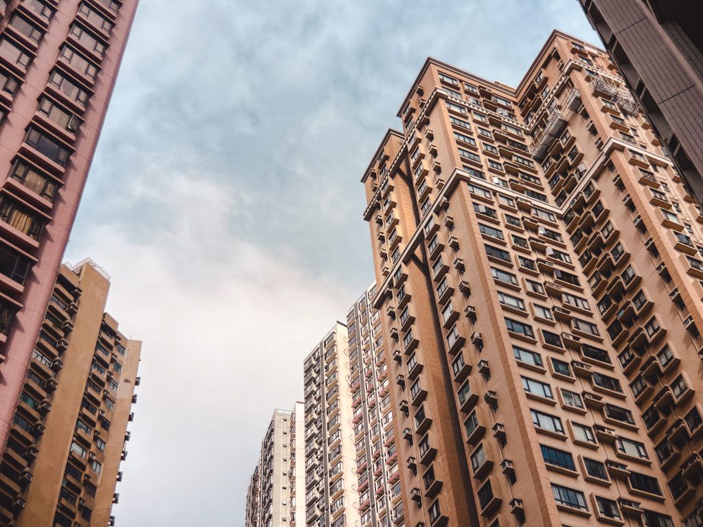 Tall, densely packed apartment buildings rise against a cloudy sky, creating an urban skyline.